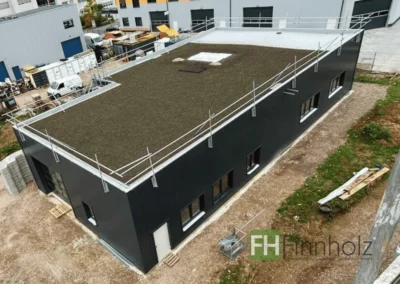 Gewerbehalle in Heidelberg - Bild 1: Die Holzhalle ist fertig. Das Bild zeigt eine Außenaufnahme des Gebäudes aus der Vogelperspektive. Die Fassade der Halle ist schwarz gehalten.