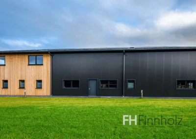 Seitenansicht der Fertigungshalle mit Büro in Soest mit Holzfassade und Hallenbereich mit dunklen Sandwichpaneelen.