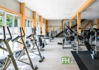 Innenansicht des Fitnessstudios in Holzbauweise mit Trainingsgeräten und sichtbaren Holzstützen.
