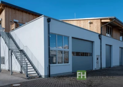 Außenansicht der Werkstatthalle mit Wohnung in Bonn mit Werkstatttoren und Putz- und Holzfassade.
