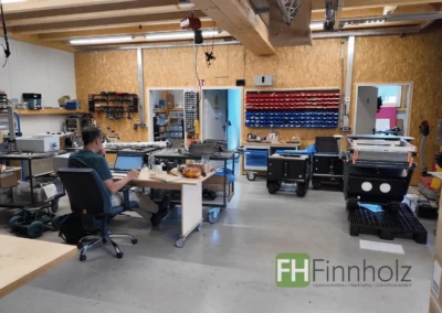 Innenansicht der Fertigungshalle mit Arbeitsplätzen, Robotiktechnik und sichtbarer Holzkonstruktion.