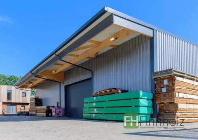 Außenansicht der Lagerhalle in Ellerau mit großem Dachüberstand, Hallentoren und gelagerten Holzprodukten.