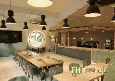 Gewerbehalle mit Gastronomie: Veranstaltungsraum mit offener Küche, großzügigen Sitzbereichen und rundem Fenster für Kochkurse und Grillevents.