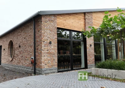 Außenansicht der Gewerbehalle in Delbrück mit Klinkerfassade, großen Glasfronten und Holzverkleidung.